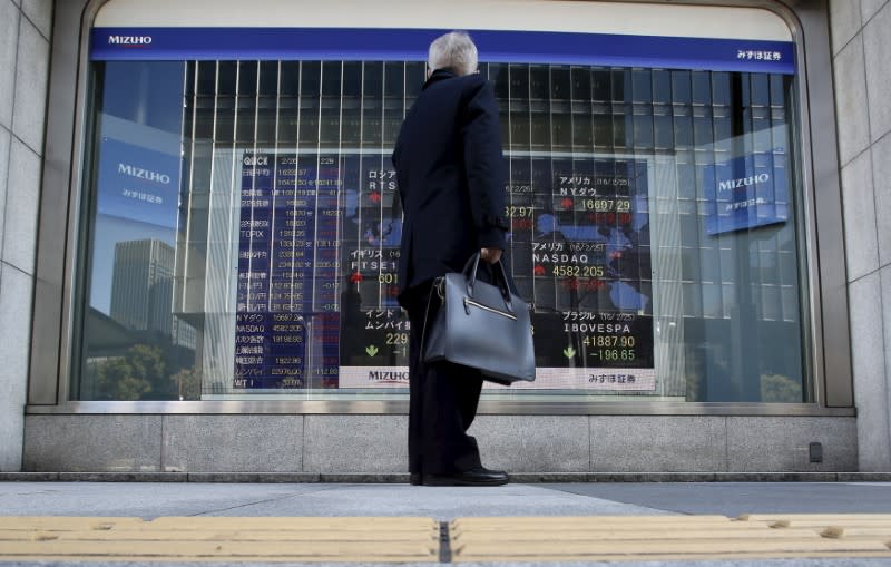 A pedestrian stands to look at an electronic board showing the stock market indices of various countries outside a brokerage in Tokyo, Japan, February 26, 2016. REUTERS/Yuya Shino