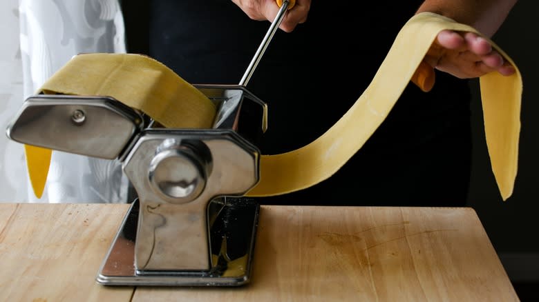 Hands making pasta with a pasta machine