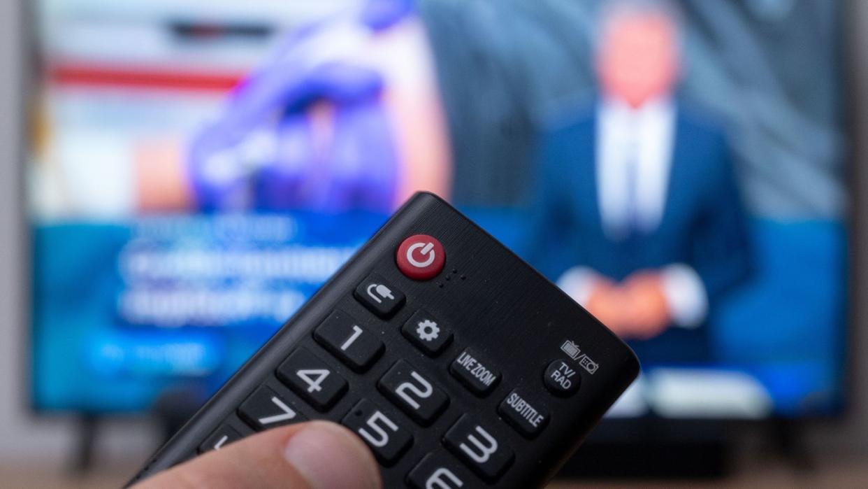 Ein Mann hält eine Fernbedienung vor einen Fernseher, auf dem die Tagesschau läuft. (Symbolbild)