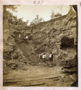 Photograph shows two white men overseeing African American men hammering boulders as others walk with wheelbarrows in a shallow pit phosphate mine, Dunnellon, Florida, 1890. (Library of Congress via AP)