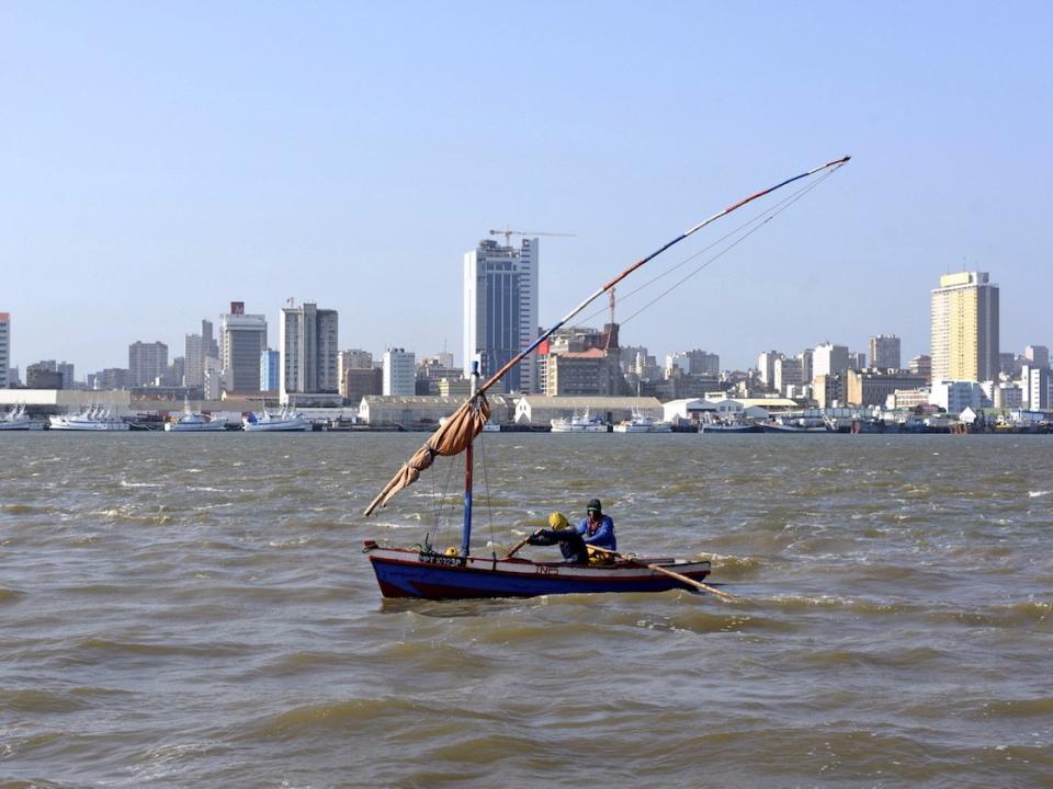 Traditional fishing boats sail as Mozambique's tuna fleet sits in dock beneath Maputo's skyline, in this picture taken August 15, 2015.