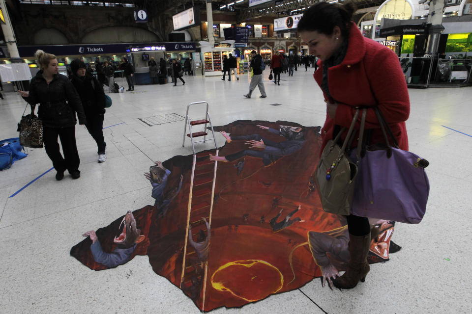 A commuter checks her step as she walks past a 3D art exhibit "Escape the Rat Race' painted on the concourse of Victoria railway station in London to promote a pest control company, Wednesday, Jan. 18, 2012. (AP Photo/Sang Tan)