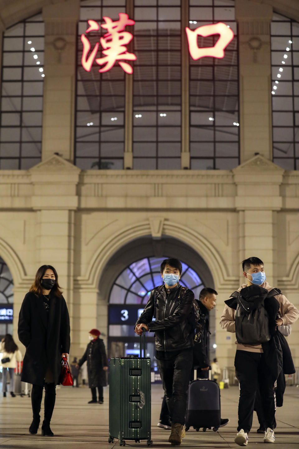 In this Jan. 21, 2020, photo, passengers wearing protective masks walk outside Hankou Railway Station in Wuhan in central China's Hubei province before authorities seals the city. For weeks after the first reports of a mysterious new virus in Wuhan, people poured out of the central Chinese city, cramming onto buses, trains and airplanes as the first wave of China's great Lunar New Year migration broke across the nation. Some carried with them a new virus that has claimed over 560 lives and sickened more than 28,000 people. (Chinatopix via AP)