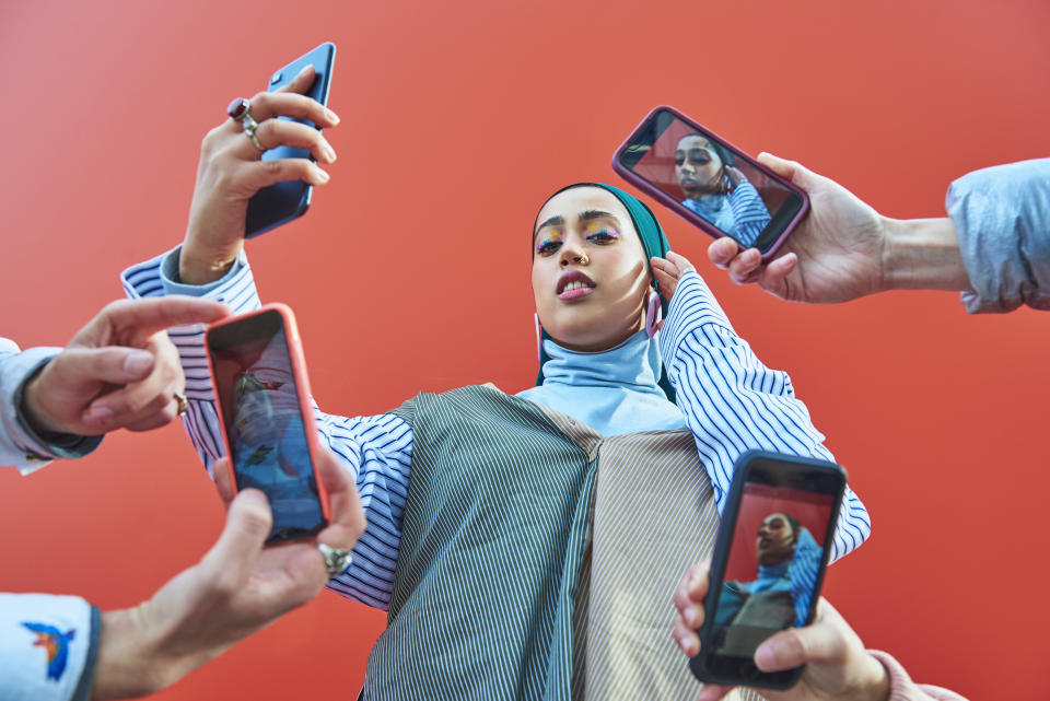 Young woman having picture taken by multiple smartphones.