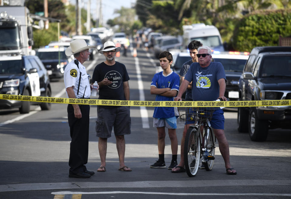 Residents wait behind police tape on the street above the site of a cliff collapse at a popular beach Friday, Aug. 2, 2019, in Encinitas, Calif. At least one person was reportedly killed, and multiple people were injured, when an oceanfront bluff collapsed Friday at Grandview Beach in the Leucadia area of Encinitas, authorities said. (AP Photo/Denis Poroy)