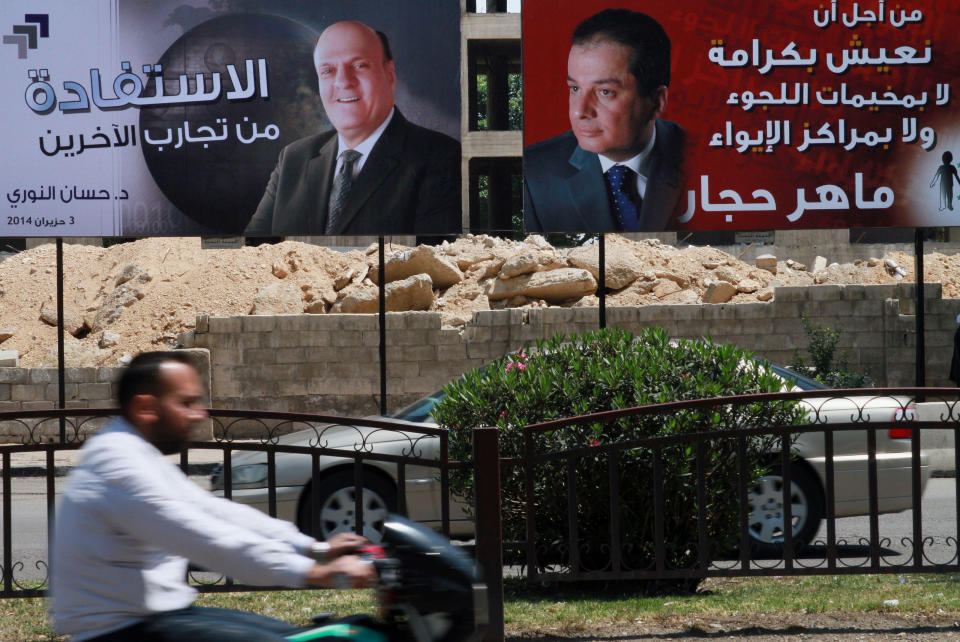 Syrian people drive by campaign posters of presidential candidates in Damascus, Syria, Monday, May 12, 2014. The Arabic, right, reads, "For us to live with dignity, neither in refugee camps nor in shelters, Maher Hajjar." The one at left reads, "There's a benefit in trying others, Hassan al-Nouri, June 4, 2014." On billboards and in posters taped to car windows, new portraits of President Bashar Assad filled the streets of Damascus on Sunday as Syria officially opened its presidential campaign despite a crippling civil war that has devastated the country and left large chunks of territory outside of government control. Assad faces two other candidates in the race: Hajjar and al-Nouri. (AP Photo)