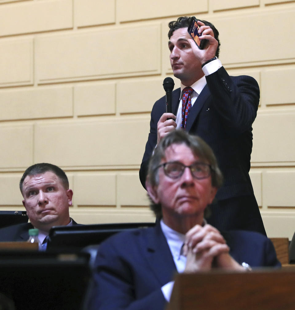 FILE- In this March 12, 2019, file photo Rhode Island House Minority Leader Blake A. Filippi holds up his mobile phone as he addresses legislators during a late afternoon session on gaming at the State House in Providence, R.I. As lawmakers nationwide decide whether to allow sports betting in their state, they’re debating whether bets, like almost everything else in our lives, can be managed online or whether wagers should be made only in person. (AP Photo/Charles Krupa, File)
