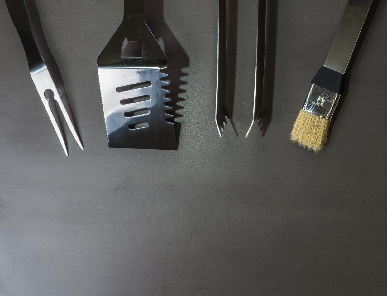 Stainless steel bbq tools on a grey stone table.