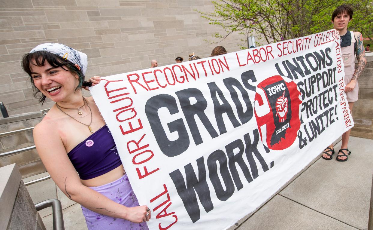 Indiana University undergraduate student Mia Holtzman, left, and graduate student Joe Simmons, right, hold a sign outside of Ballentine Hall on campus during the graduate student worker strike on Wednesday, April 17, 2024.