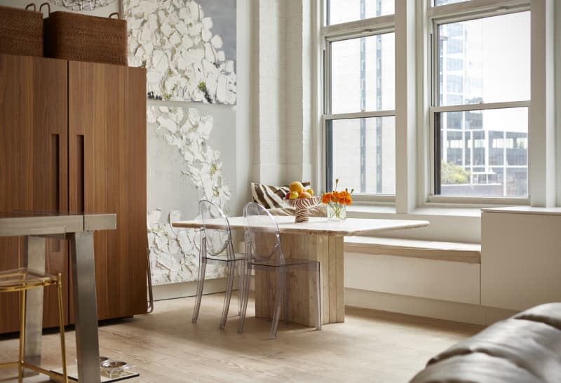 Marble table topped with a bowl of fruit and flowers in light filled apartment.