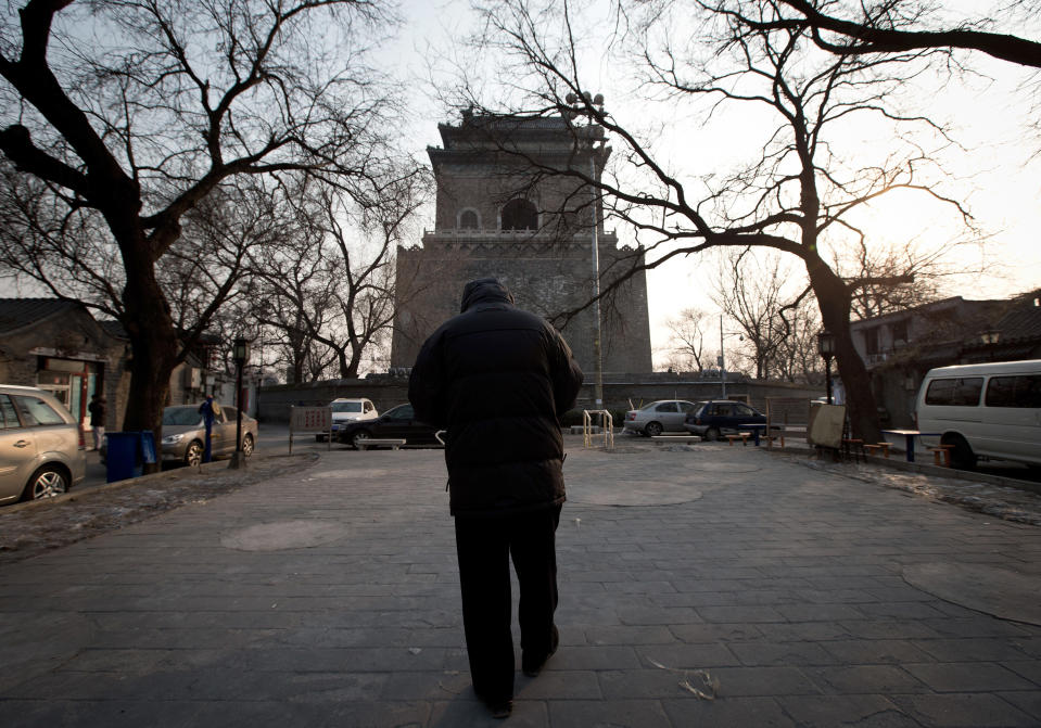 In this photo taken on Dec. 26, 2012, a Chinese man walks on the square near the historical Drum and Bell Tower, seen in the background, in Beijing. In a corner of old Beijing, behind two well-known landmarks, the sun may soon set for the last time on dozens of scuffed courtyard homes in a plan to recreate a piece of the country’s glorious dynastic past.(AP Photo/Andy Wong)