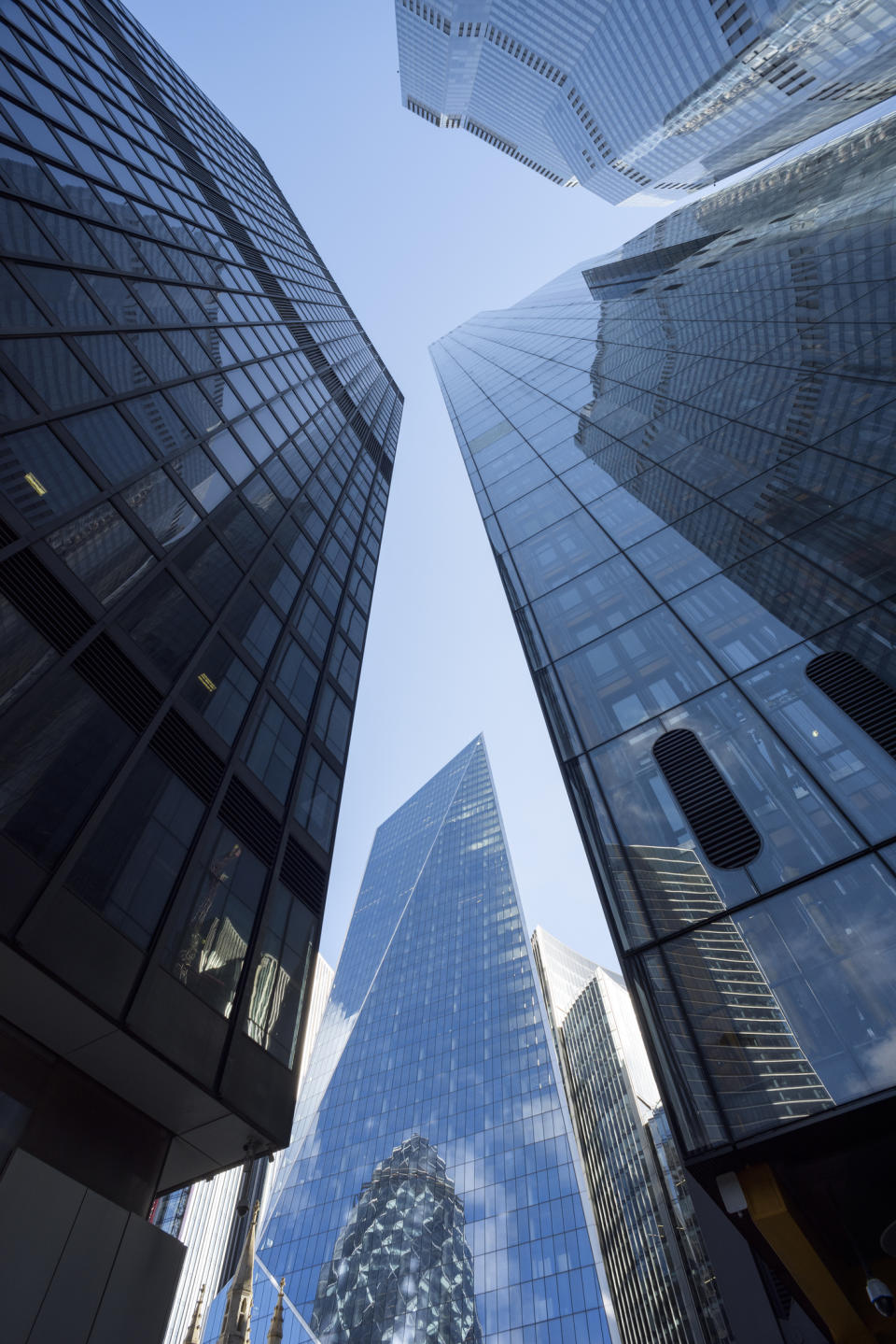 View looking up at modern skyscrapers from a low angle, showcasing the architecture and glass reflections in a city business district. No people are in the image