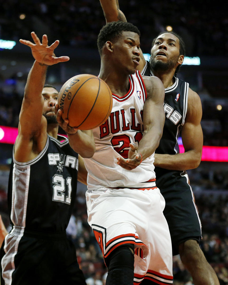Chicago Bulls shooting guard Jimmy Butler (21) passes in front of San Antonio Spurs power forward Tim Duncan, left, and small forward Kawhi Leonard, right, during the second half of an NBA basketball game on Tuesday, March 11, 2014, in Chicago. (AP Photo/Andrew A. Nelles)