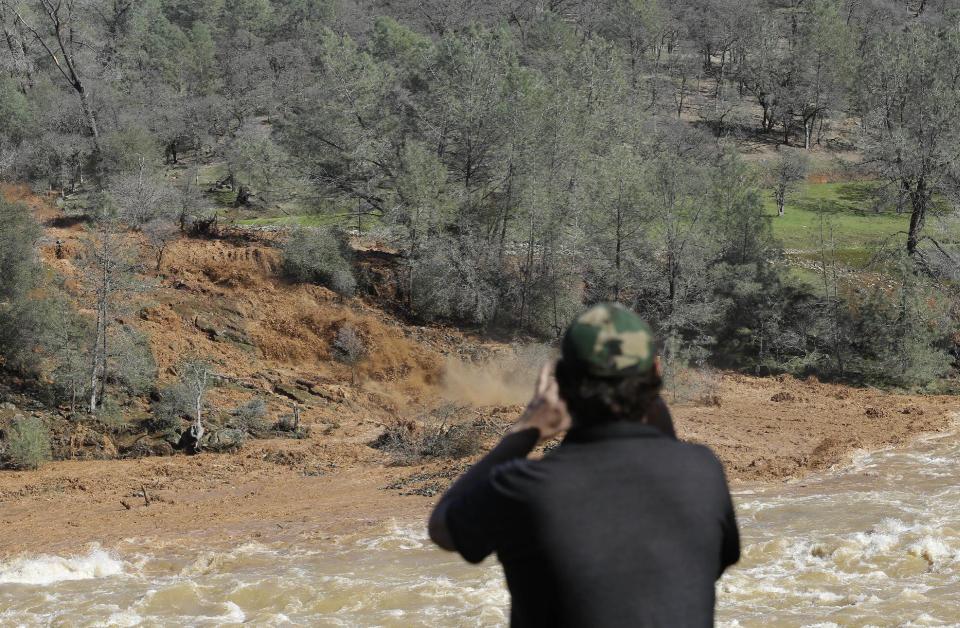 <p>E. Knight uses his smartphone to record muddy water rushing down the emergency spillway at Oroville Dam, Saturday, Feb. 11, 2017, in Oroville, Calif. Water started flowing over the emergency spillway at the nation’s tallest dam for the first time Saturday after erosion damaged the Northern California dam’s main spillway. (AP Photo/Rich Pedroncelli) </p>