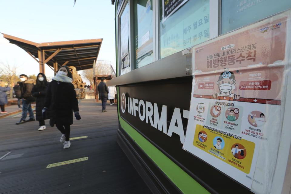 People wearing face masks pass by a poster about precautions against the coronavirus as they visit to celebrate New Year at Imjingak in Paju, near the border with North Korea, South Korea, Friday, Jan. 1, 2021. The poster reads: "Precautions against the coronavirus." (AP Photo/Ahn Young-joon)