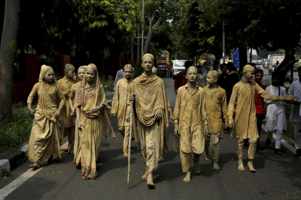 School children dressed as statues, depicting Indian freedom leader Mahatma Gandhi's Dandi March, cross a road to perform at a traffic intersection on the eve of Gandhi's 150th birth anniversary in New Delhi, India, Tuesday, Oct. 1, 2019. Dandi March is the name given to the Salt Satyagraha (Salt March) where Gandhi and other freedom fighters marched 241 miles to the sea to make their own salt on April 6, 1930 as an act of civil disobedience against the British colonial rule. (AP Photo/Altaf Qadri)