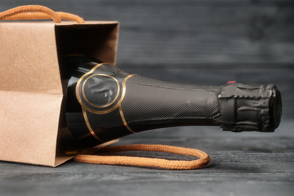 Sparkling wine in craft gift bag on black wooden background. Toned image with selective focus