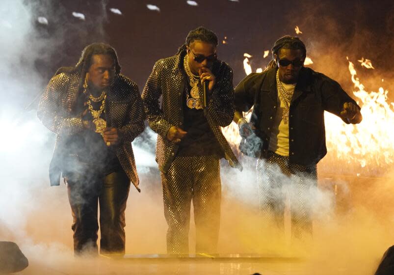 Three men in black outfits performing on a foggy stage