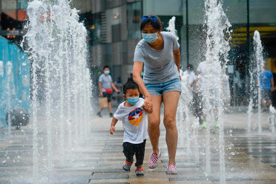 A woman and a child wearing face masks walk past a row of fountains in a business district in Beijing on June 28, 2020. Chinese health officials said on June 28 that Anxin county about 90 miles from Beijing, will be "fully enclosed and controlled", the same strict measures imposed at the height of the pandemic in the city of Wuhan earlier this year. 