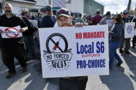 Alec Young, a shipfitter at Bath Iron Works, center, demonstrates against COVID-19 vaccine mandates outside the shipyard on Friday, Oct. 22, 2021, in Bath, Maine. Some American workers are making the painful decision to quit their jobs and abandon cherished careers in defiance of what they consider intrusive mandates requiring all businesses with 100 or more workers require employees to be fully vaccinated or undergo weekly testing. (AP Photo/Josh Reynolds)