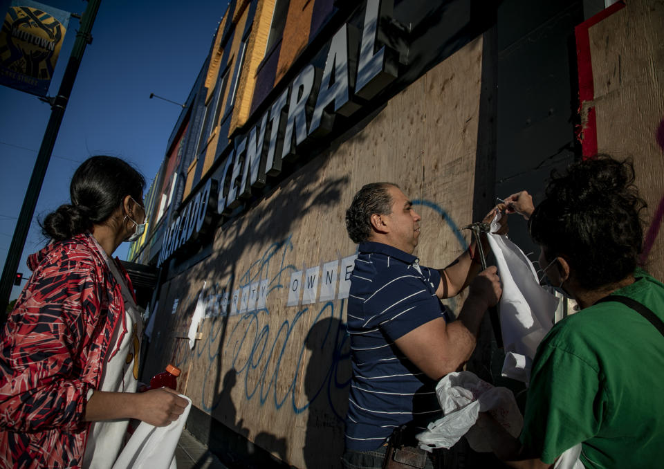 Saturday, May 30, 2020 - business owners from Minneapolis' Mercado Central, a cooperative of largely Latino-owned businesses on Lake Street, nail pieces of white cloth onto the boarded-up building as a symbol of peace and a possible deterrent against rioting, in Minneapolis. The destruction caused by vandals and looters, who struck as demonstrators took to the streets in reaction to the killing of George Floyd,  has devastated small businesses already reeling from the coronavirus outbreak. (AP Photo/Bebeto Matthews)