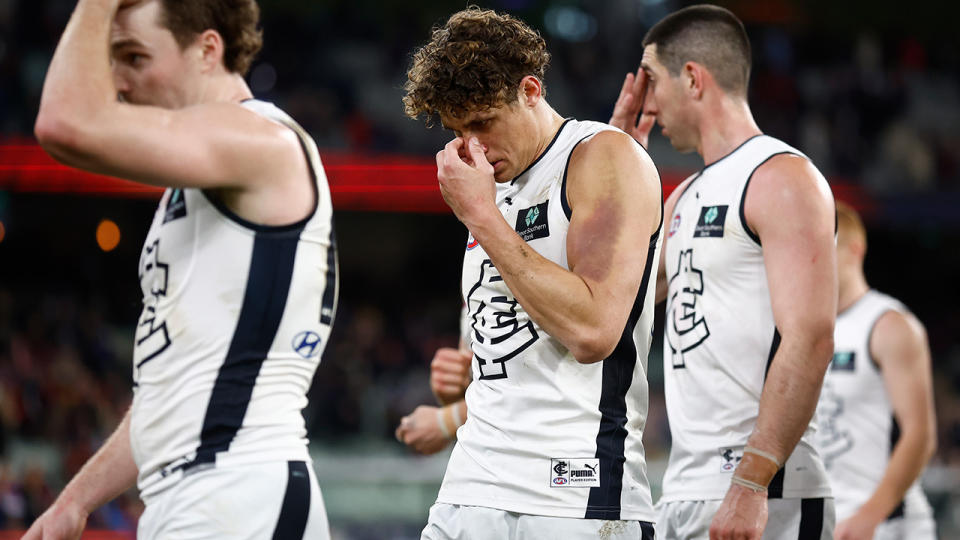 Carlton player Charlie Curnor rubs his head as players walk off the ground.