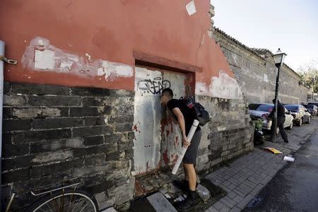 Chinese artist ROBBBB checks a closed door before he pastes his work in a traditional alleyway, or "hutong", in central Beijing September 25, 2015. REUTERS/Jason Lee