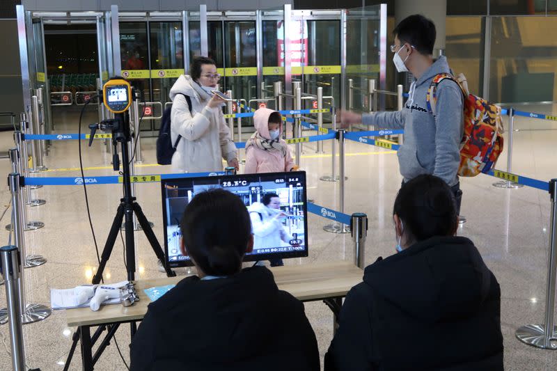 Staff members monitor thermal scanners that detect temperatures of passengers who have just landed, at the arrival terminal in Beijing Capital International Airport