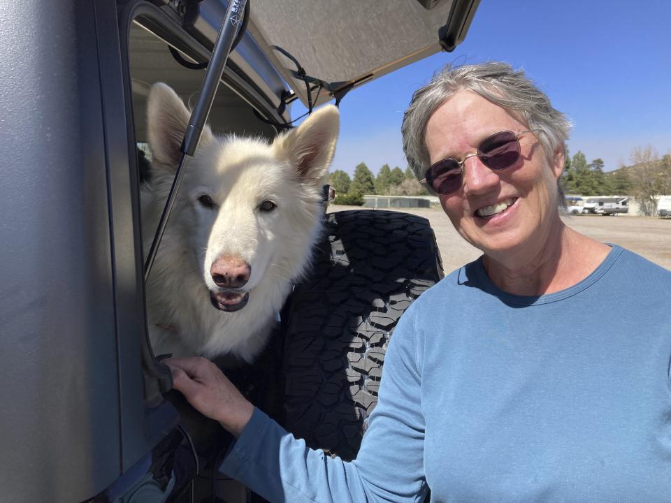 Lisa Wells, stands with her dog Lily, as they wait for family in the parking lot on the outskirts of Flagstaff, Ariz., on Wednesday, April 20, 2022. Wells and her family evacuated because of a wildfire that destroyed their home. (AP Photo/Felicia Fonseca)