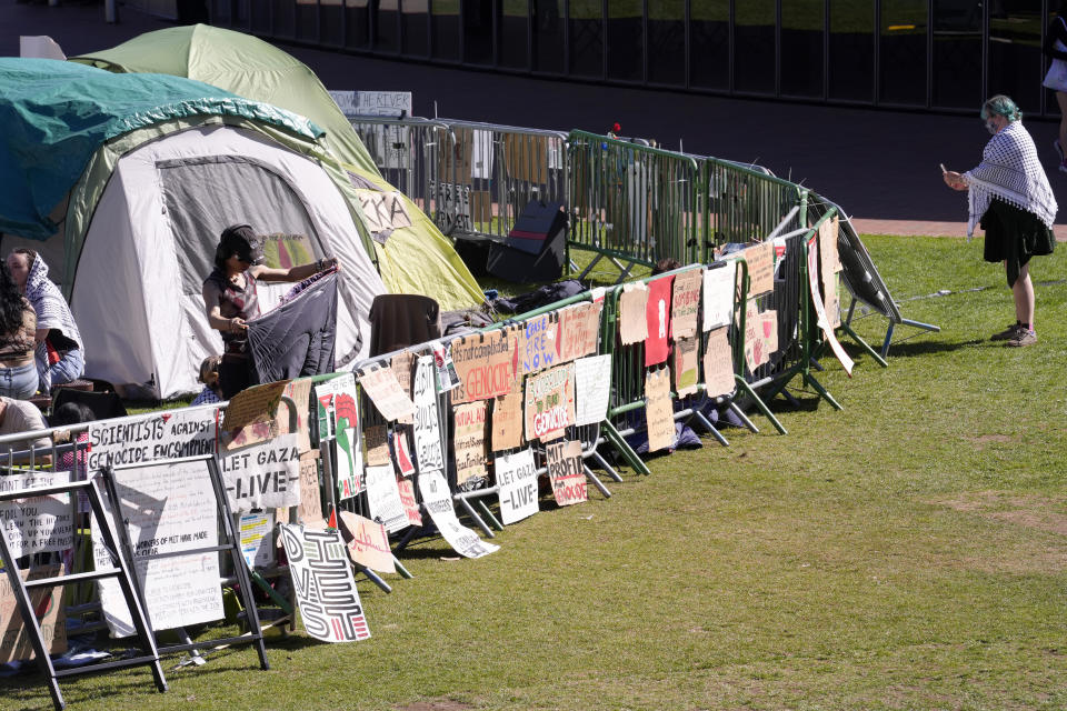 A passer-by, right, uses a mobile device to record a barrier with placards at an pro-Palestinian encampment of tents on the campus of Massachusetts Institute of Technology, Tuesday, May 7, 2024, in Cambridge, Mass. Students at MIT set up the encampment to protest what they said was MIT's failure to call for an immediate ceasefire in Gaza and to cut ties to Israel's military. (AP Photo/Steven Senne)