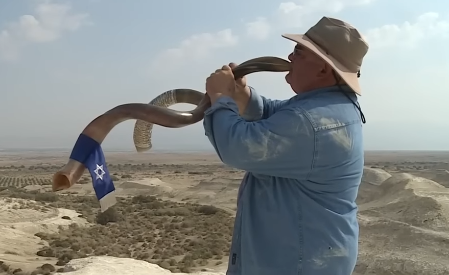 Man blowing a shofar in a desert landscape with an Israeli flag nearby; title reads 