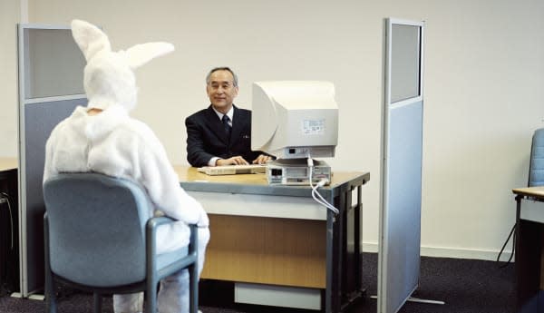 Man wearing rabbit suit at desk opposite mature businessman