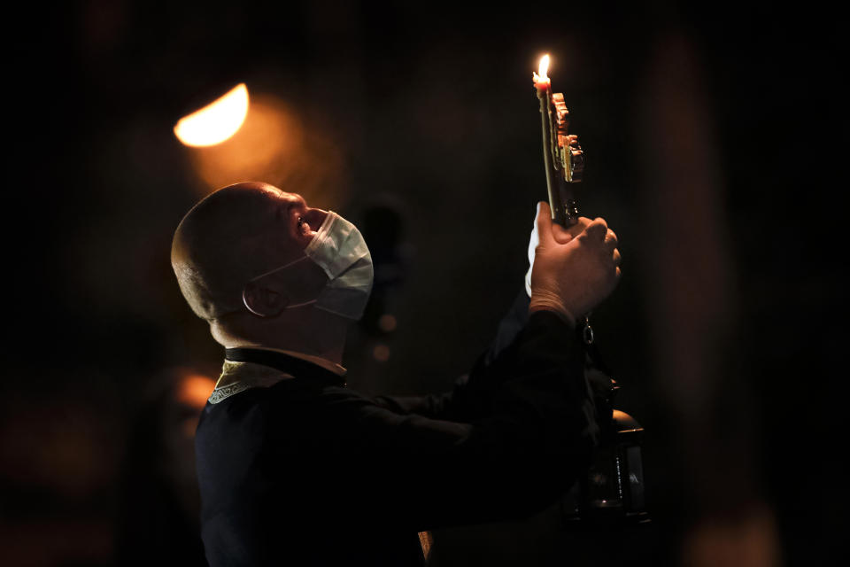 A priest blesses worshipers that stand at the windows of an apartment block during the coronavirus outbreak in Bucharest, Romania, Saturday, April 18, 2020. Priests accompanied by volunteers distributed the holy light ahead of the usual time, at midnight, as people observed the interdiction to join religious celebrations in the week leading to the Orthodox Easter, imposed across Romania as authorities try to limit the spread of the COVID-19 infections. (AP Photo/Vadim Ghirda)