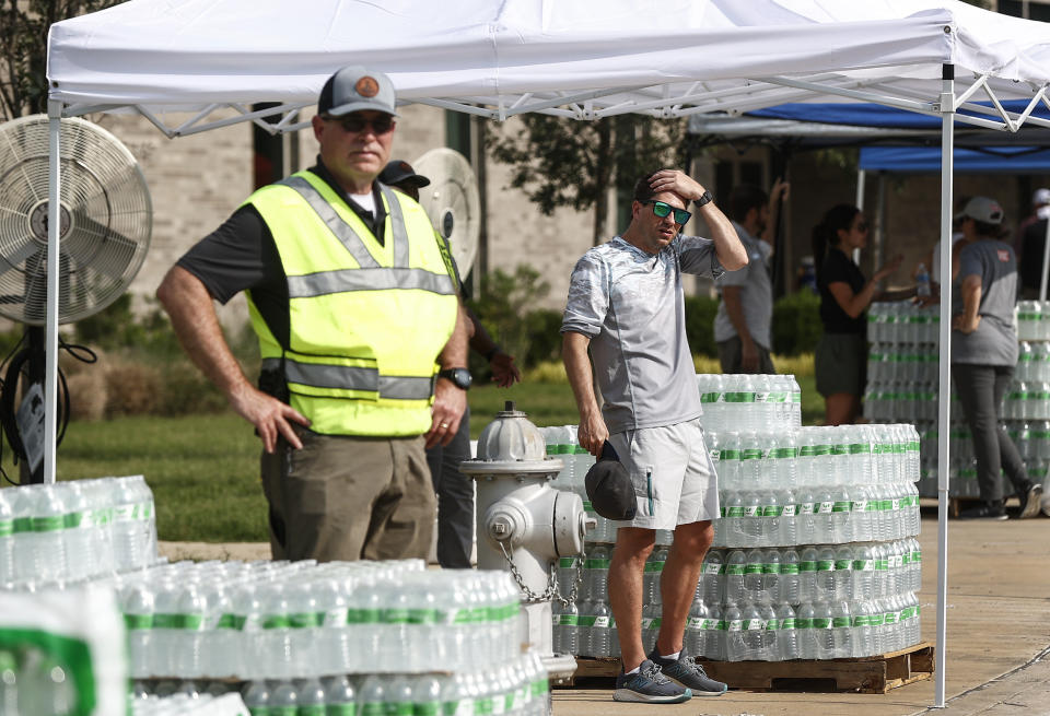 People stand by cases of bottled water as the City of Germantown gives them out to residents on Monday, July 24, 2023 at Forest Hill Elementary School in Germantown, Tenn. Residents of the Tennessee city were told that diesel fuel spilled into a local reservoir, and to avoid drinking tap water. People remain under an order Wednesday, July 26 to avoid using water for everything except flushing toilets. They can’t drink or boil tap water, or use it showering or bathing. (Mark Weber/Daily Memphian via AP)