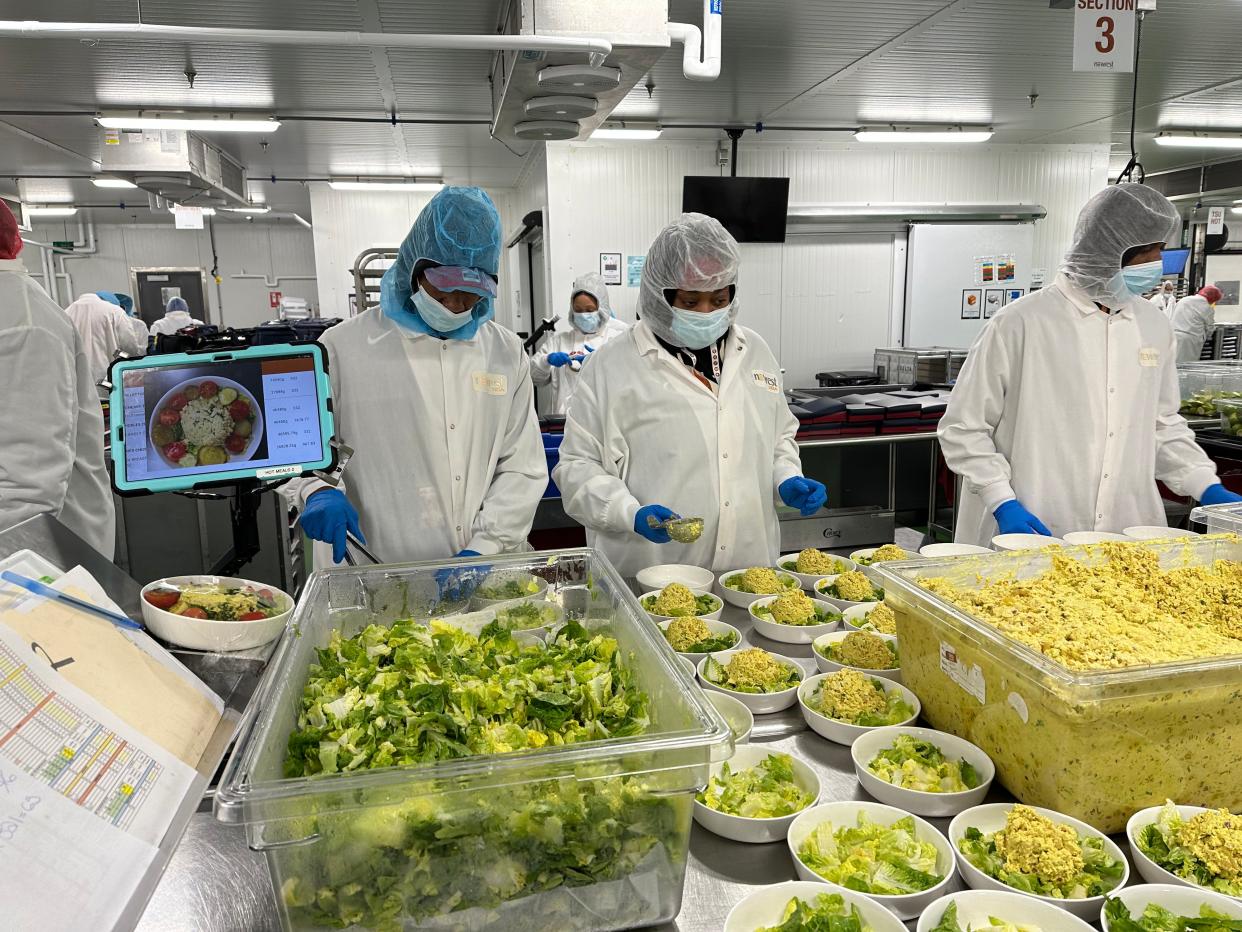 A plating team using calibrated scoops to dole out curry chicken salad.