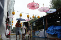 Residents cover up with umbrellas as they walk past stalls closed during a rainy day in Beijing, Sunday, Aug. 14, 2022. (AP Photo/Ng Han Guan)