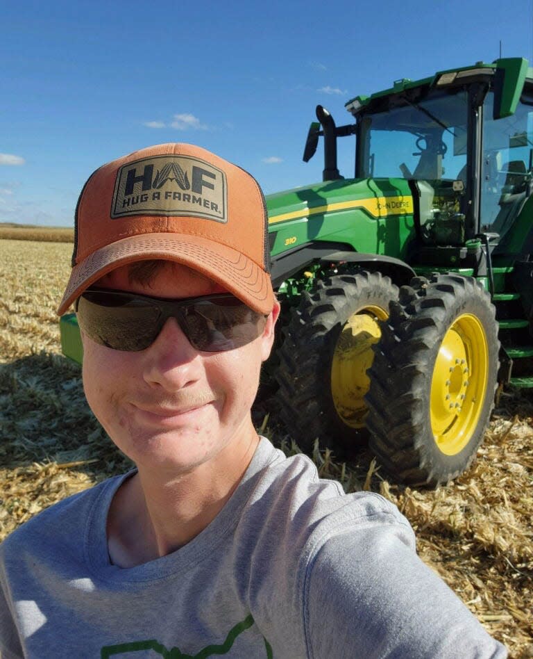 Cooper Meshew stands in front of a John Deere tractor in a cornfield he is harvesting out west.