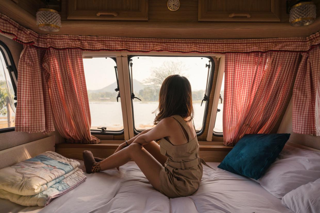 Beautiful young asian woman relaxing and looking the view in motor home on campsite at evening