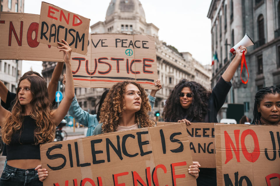 Four individuals holding signs with messages advocating for justice, peace, and an end to racism during a protest