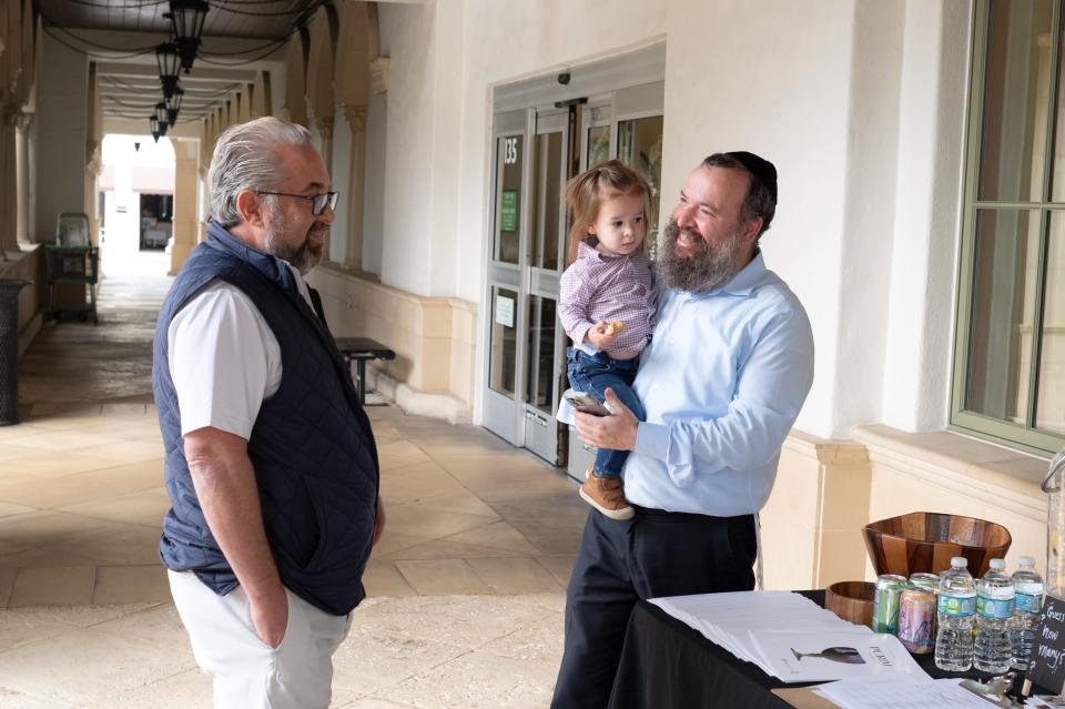 Rabbi Zalman Levitin, holding his son Yaisef, talks with Marc Taub during a past Chabad House Purim at Publix.
