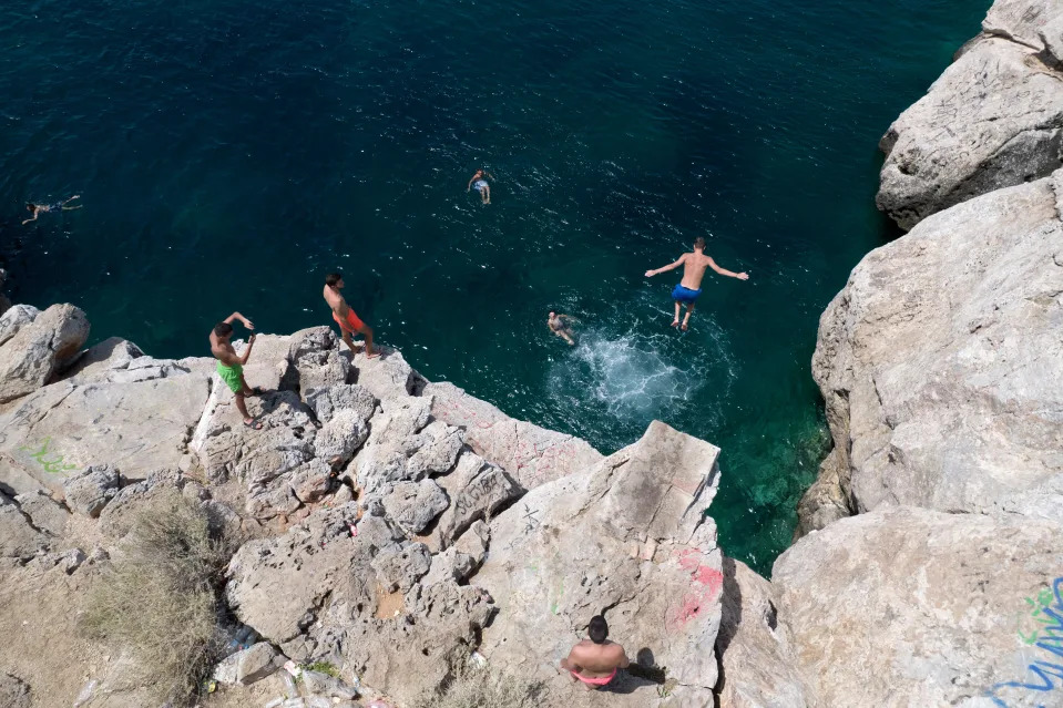 A youth jumps in the sea from a rock at Varkiza village, a few miles southwest of Athens, on Thursday, July 29, 2021.