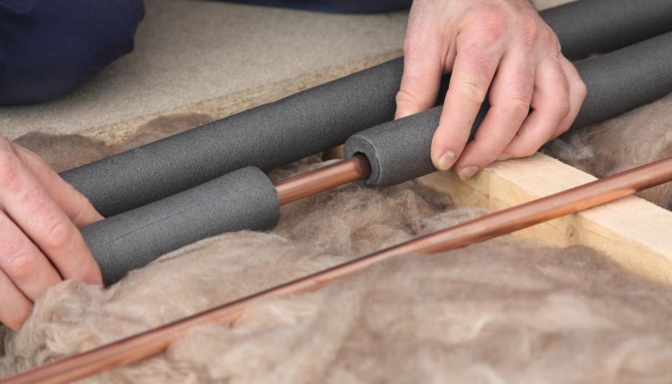 Person wrapping copper pipes with grey foam insulation