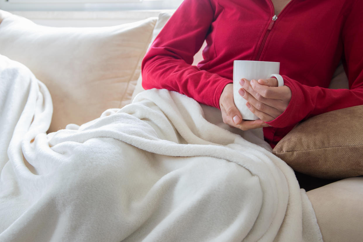 Crop view of young adult woman is relaxing on comfortable sofa with hot beverage. Cozy lazy time indoor. Cold seasons - cold and flu