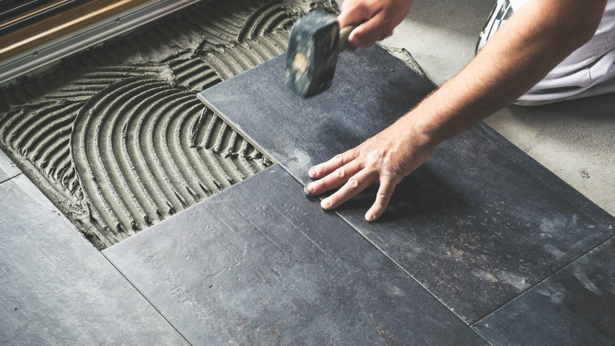 Worker carefully placing ceramic floor tiles on adhesive surface.