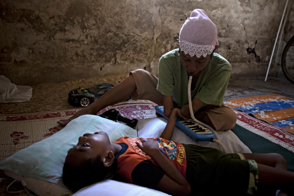 Armless professional photographer Rusidah, 44, plays melodica to her nephew Dayat inside her house cum studio on March 13, 2012 in Purworejo, Indonesia. Dayat, 12, has been paralyzed since birth and now lives with Rusidah. (Photo by Ulet Ifansasti/Getty Images)