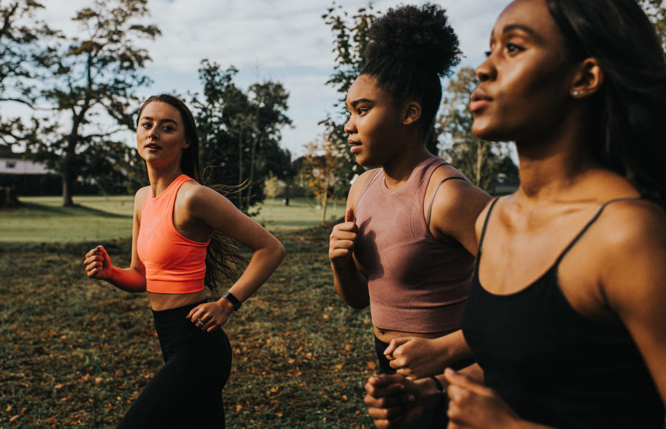 Group of woman train in a sunny park. Personal trainer shouts instructions and affirmations at her clients as they jog.