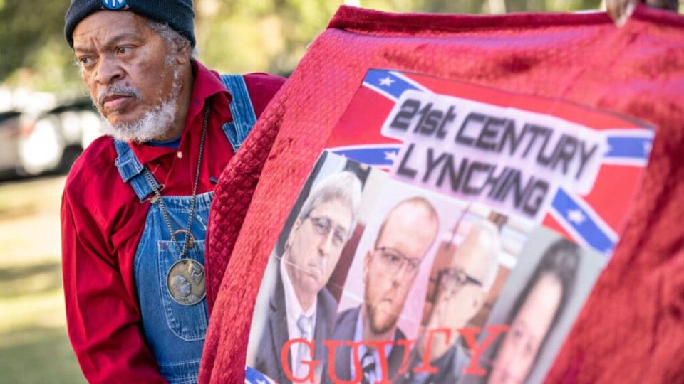 Eric Terrell, vice president of the National Action Network, holds a banner with photos of William Roddie Bryan, Travis McMichael, Greg McMichal and former Brunswick District Attorney Jackie Johnson outside the Glynn County Courthouse as the jury deliberates in the trial of the killers of Ahmaud Arbery on November 24, 2021 in Brunswick, Georgia. (Photo by Sean Rayford/Getty Images)