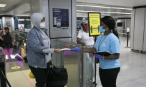 Shaquanna Parnell, right, with the Mayor's Office of Public Engagement, hands an information leaflet to a passenger arriving at Amtrak's Penn Station, Thursday, Aug. 6, 2020, in New York. Mayor de Blasio is asking travelers from 34 states and Puerto Rico, where COVID-19 infection rates are high, to quarantine for 14 days after arriving in the city. (AP Photo/Mark Lennihan)