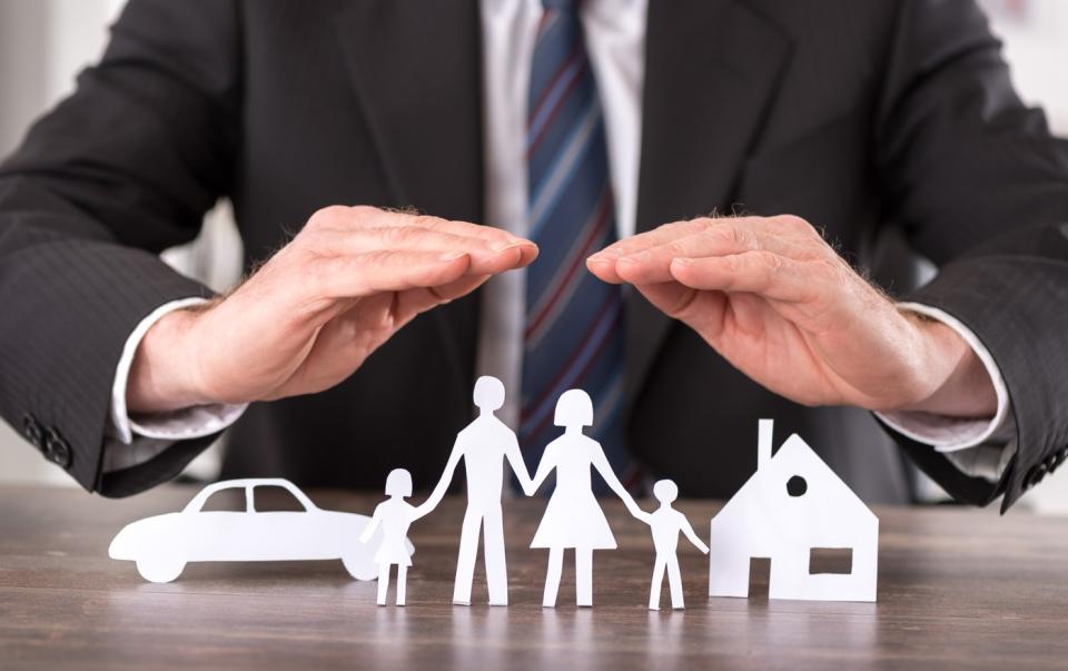 A businessman places his hands on paper cutouts of a family, a house, and a car.