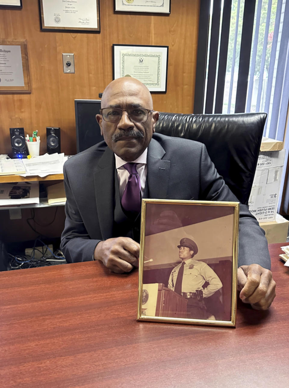 Attorney David A. Robinson holds a photo in his Southfield, Mich., office, Oct. 10, 2023, taken when he served as a Detroit police officer. Robinson spent 13 years as an officer. Now, most of his clients are Blacks who allege harassment and civil rights violations by police. He says lying by officers to citizens a "great disappointment." "Because people hold police in high esteem," said Robinson. (AP Photo/Corey Williams)